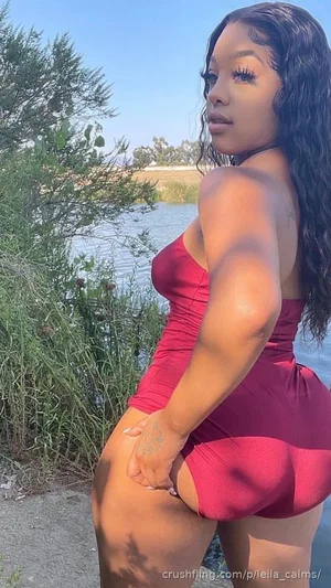 Woman in red one-piece swimsuit posing by water, outdoor setting.