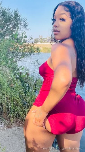 Woman in red one-piece swimsuit posing by water, outdoor setting.