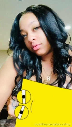 Woman with long black wavy hair, wearing necklace with 'R' pendant, holding yellow object with