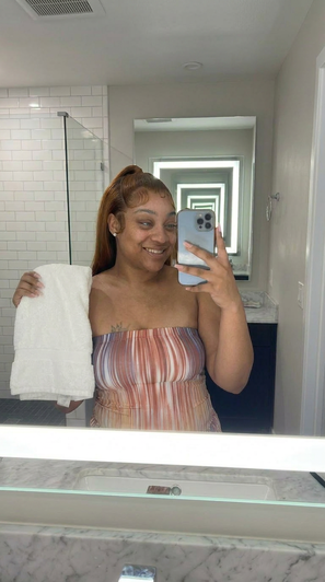 Woman in striped top holding towel, taking mirror selfie in bathroom.