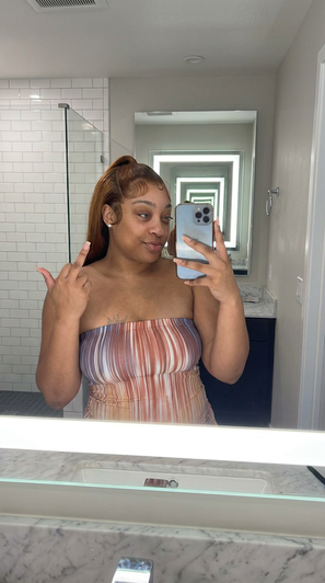 Woman in striped strapless top taking mirror selfie in bathroom.