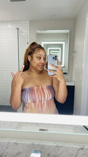 Woman in striped strapless top taking mirror selfie in bathroom.