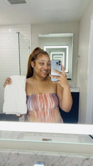 Woman in striped top holding towel, taking mirror selfie in bathroom.