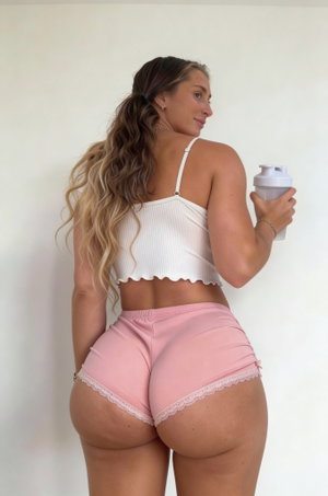 Curvy woman in white crop top and pink shorts holds shaker indoors.