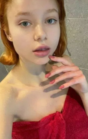 Woman with red hair wrapped in red towel, standing in tiled room.