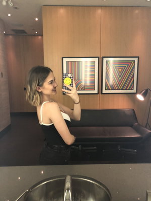 Woman with short hair in black and white top takes mirror selfie in modern room with art and