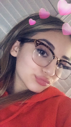 Woman with glasses and pink heart filters wearing a red hoodie indoors.