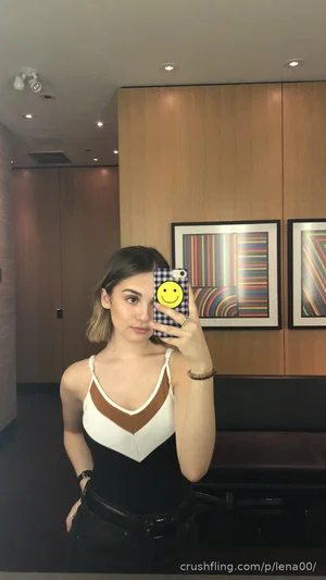 Woman in black and white top taking mirror selfie in modern indoor setting.
