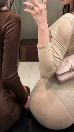 Woman in sheer beige dress taking mirror selfie indoors.