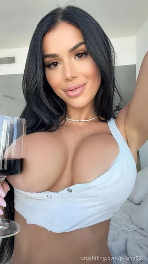 Woman with long black hair in a light blue crop top holding a wine glass indoors.
