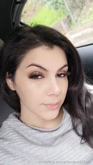 Woman with dark hair and makeup wearing a gray striped top in a car.
