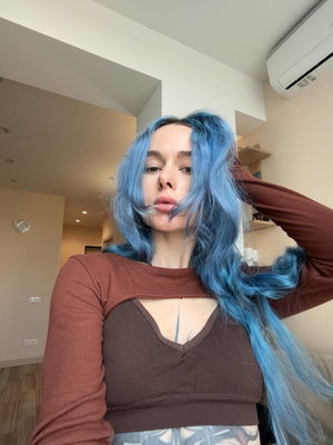 Blue-haired woman in brown cutout top taking indoor selfie.