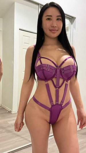Woman with long black hair in purple lingerie posing indoors.