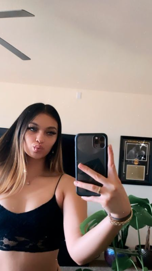 Woman with long hair in black crop top taking mirror selfie in bedroom.