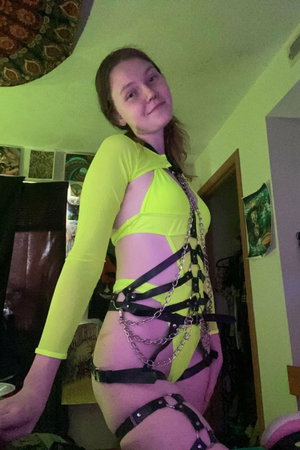 Woman in neon yellow top and black harness posing indoors.
