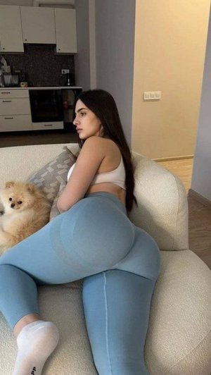Woman in blue leggings and white top on couch with dog.