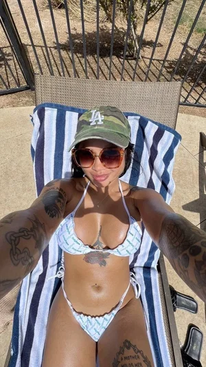 Woman in patterned bikini and cap lounging on striped towel outdoors, tattoos visible.