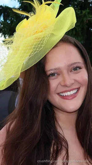 Woman with long brown hair wearing a yellow fascinator hat, smiling outdoors.