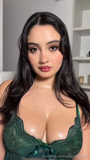 Woman with long dark hair wearing green lace lingerie, indoors, facing camera.