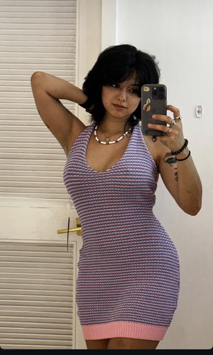 Asian woman in purple knit dress poses in bathroom mirror.