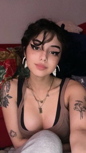 Curvy woman with tattoos in tank top and sweatpants on bed.