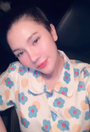 Woman with short hair in floral shirt, sitting in car, looking at camera.