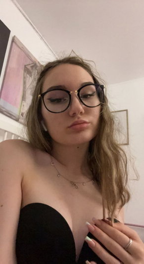 Woman with glasses and wavy hair wearing black top, indoors.
