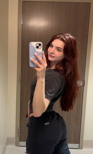 Redhead woman in black scrubs mirror selfie indoors.