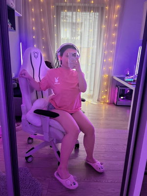 Woman in pink shirt taking selfie in gaming chair indoors.