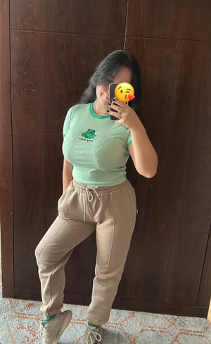 Woman in green crop top and beige pants poses for mirror selfie indoors.