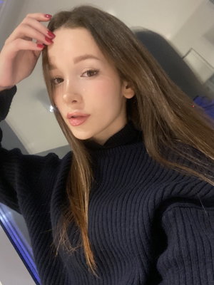 Woman with long brown hair in dark sweater taking indoor selfie.