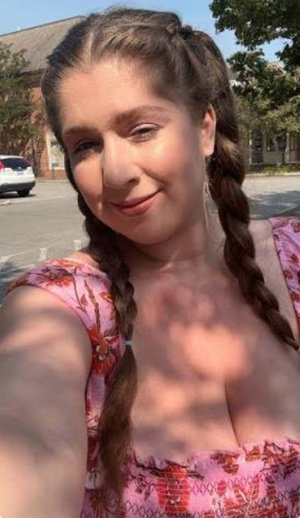 Woman with braided hair in pink floral top taking outdoor selfie.