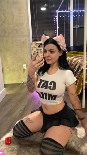 Curvy woman with black hair, cat ears, crop top, mini skirt, stockings in bedroom.