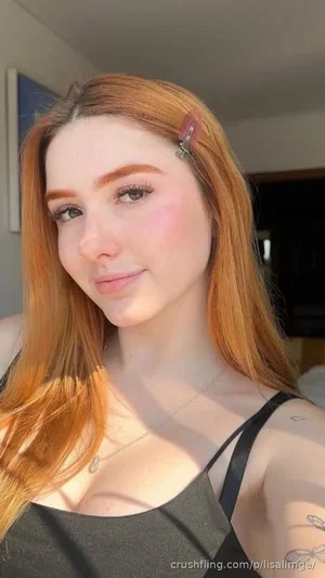 Woman with red hair, black top, tattoos on arm, indoors, soft lighting.