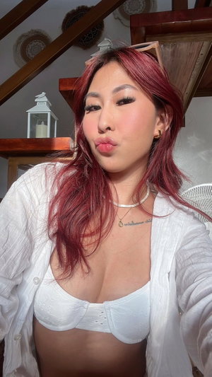Woman with red hair in white bra and open shirt, making playful face indoors.