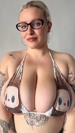 Woman with tattoos wearing a cartoon-print bikini top, indoors, facing camera.