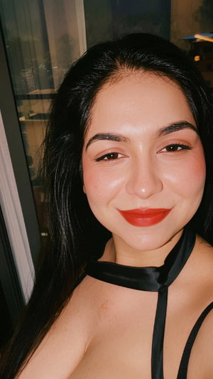 Woman with long dark hair and red lipstick wearing black halter top indoors.