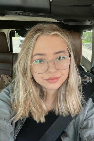 Blonde woman with glasses in hoodie inside car.
