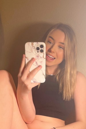 Blonde woman in black crop top taking indoor selfie.