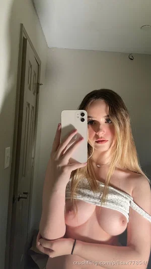 Woman with long hair in off-shoulder top taking mirror selfie in indoor setting.
