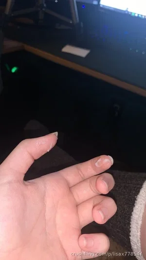 Close-up of a hand with chipped nail polish, wearing a dark sweater, in a dimly lit indoor setting.