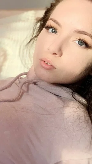 Woman with blue eyes and dark hair lying down, wearing a light purple top, indoors.