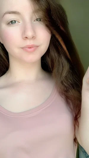 Woman with long brown hair wearing a pink tank top indoors.