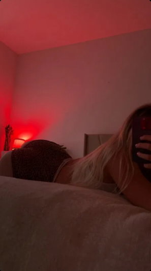 Blonde woman in leopard print shorts lying on bed under red light.