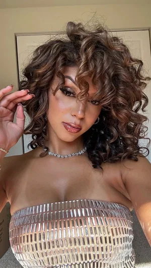 Woman with curly hair wearing a shiny strapless top indoors.