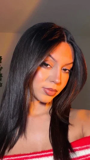 Woman with long black hair wearing red and white off-shoulder top, indoor setting.