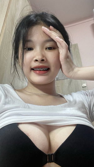 Asian woman in black bra under white top in bathroom.