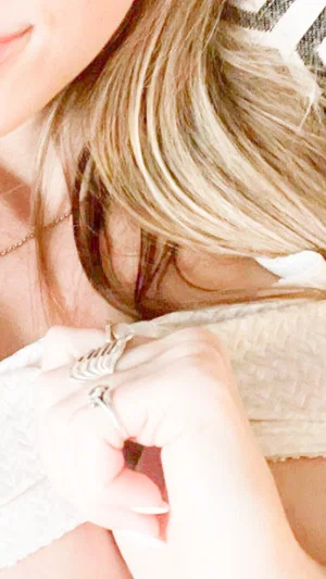 Woman with blonde hair wearing white top, close-up of hand with rings.