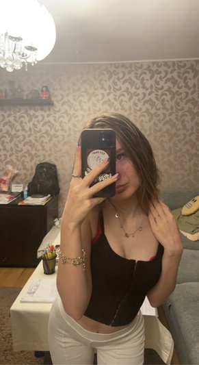 Woman in black top and white pants taking selfie indoors.