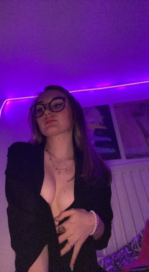 Brunette woman with glasses in open black blazer under purple lights.